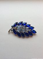 Front view of the leaf-shaped brooch with dark and light blue marquise rhinestones set in silver tone metal.