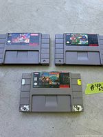 Photo of three Super Nintendo game cartridges: Darkwing Duck by Capcom, Sonic Blast by Sega, and Donkey Kong Country 2 by Nintendo. Cartridges show typical label wear; Donkey Kong cartridge has corner label damage and price sticker.