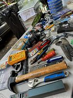 Photo showing a variety of hand tools including hammer, wrenches, screwdrivers, multimeter, and pliers laid out on a surface.