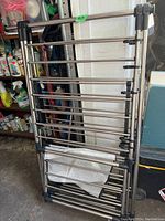 Photo of a folded stainless steel clothes rack with multiple horizontal bars and black plastic connectors, placed in a garage setting.