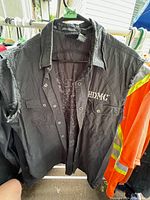 Black Harley Davidson men's sleeveless cotton vest on hanger with HDMC logo on chest and metal snap buttons.