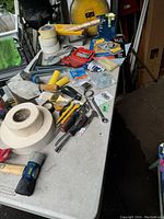 Overview of various tools and hardware laid out on a table, including hammers, measuring tapes, wrenches, tape rolls, screwdrivers, and hardware.