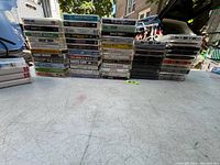 Photo showing stacks of original cassette tapes on a table outside, displaying multiple titles and cases of various artists and music genres.