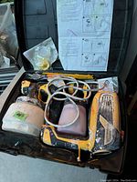 Close-up photo of the opened black plastic carrying case showing the yellow Wagner paint sprayer with two attached containers and hoses along with instruction sheet inside the lid.