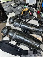 Grey Empire chest protector, Rawlings catcher's mask, and black Rawlings shin guards with knee pads displayed on a table along with black socks.