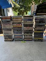 Photo shows four stacks of cassette tapes arranged on a concrete floor. Titles of tapes visible, including various artists and genres from rock, country, pop.
