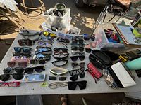 Wide overhead view of all glasses laid out on a table showing various styles of sunglasses, eyeglasses, and eyeglass cases.