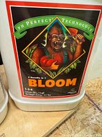 White 23L plastic container of Advanced Nutrients Bloom fertilizer showing front label with gorilla holding tomato and wine glass, nutrient ratio 1-3-4, and pH Perfect technology.