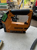 Side view of a new Bostitch air stapler on a white surface outdoors, showing detailed view of the tool body and branding.