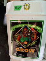 Photo shows a white 23L plastic container labeled 'Grow' fertilizer by Advanced Nutrients with colorful gorilla illustration and product details.