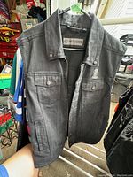 Black Harley-Davidson sleeveless vest hanging on rack, showing front and design details.