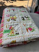 Folded quilt with alphabet blocks featuring illustrations of bees, vegetables, and characters, showing cream background and colorful prints.
