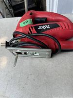 Red Skil jigsaw power tool showing side profile with blade, cord, and base plate visible.