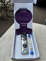 Open box showing TELUS Slimline Wi-Fi Doorbell Camera, installation guide, and mounting accessories inside the packaging.