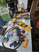 Overview of tools and hardware on a white folding table including drills, screwdriver sets, tool cases, and various hand tools