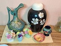 Seven items together in single view: relief ewer at left, lidded jar and small art vase at back, flower dish and three posy vases at front