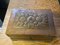 Top view showing rectangular wooden box with carved floral pattern and central eye on lid.