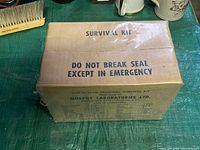 Sealed rectangular cardboard box labeled 'SURVIVAL KIT' with instructions 'DO NOT BREAK SEAL EXCEPT IN EMERGENCY'