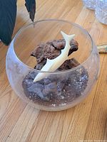 Full view of fishbowl containing the brown rock-like base and white fish sculpture inside on wooden surface.