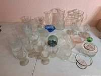 Wide angle photo of all assorted vintage glassware and crystal items on white surface showing quantity and variety.