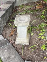 Concrete pillar in soil bed with visible weathering and plants around