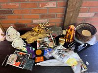 Wide view of assorted items including dishware, animal figurines, tools, and sundry pieces arranged on a table and shelf against a brick wall.