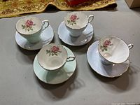 Set of four Paragon teacups and saucers arranged on a table, showing the rose floral design inside each cup and the gold trim detailing on edges.
