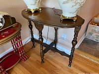 Front and angled view of the solid walnut side table showing curved oval top, four turned legs, and cross stretcher.