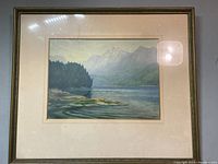 Framed watercolour painting showing full mountain scene with lake and rocky shore, signed and dated.