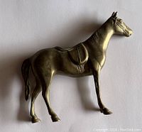 Side angled view of brass horse figurine showing details of saddle and headgear.