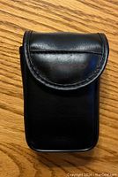 Closed black synthetic leather binoculars case on wooden surface.