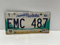 Front view of the 2010 Manitoba license plate showing license number EMC 487, 'Friendly Manitoba' text, bison logo, and registration stickers.