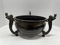 Front view of dark metal flower pot with two dragon-shaped handles and textured, hammered body on a white background.