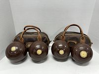 Two pairs of dark brown early championship lawn bowling balls displayed in front of their leather carrying cases