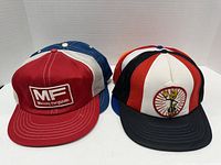 Front view of two trucker hats: red Massey Ferguson hat and white/red/black hat with cartoon character embroidered.