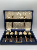 Eight brass and rosewood inlay demitasse spoons displayed inside blue hinged case with satin and velvet lining.