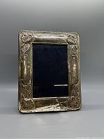 Front view of rectangular silver picture frame with floral engravings. Noticeable damage and silver wear at bottom edge.