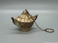 Side view of the antique sterling silver tea infuser shaped like a teapot, showing detailed perforations and attached chain with ring.