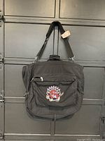 Front side of the black nylon Toronto Raptors bag showing the colorful team logo patch centered on the zipped front pocket.