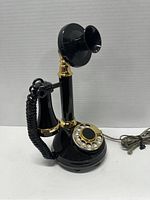 Front angled view of the black and gold 1973 Northern Telecom candlestick telephone showing handset and rotary dial.