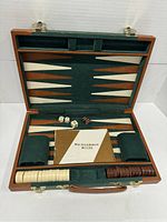 Open backgammon game board inside wooden framed case with green felt and cream/brown points. Chips, dice, and rules booklet displayed.