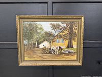 Frontal view of the vintage oil painting showing a yellow house, trees, and a horse-drawn cart. The painting is inside a gold decorative frame.
