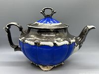 Side view of vintage porcelain tea pot showing cobalt blue body and black glaze on top with ornate handle.