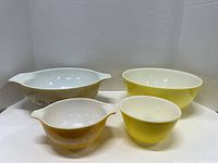 Four vintage Pyrex mixing bowls: a large speckled cream Cinderella bowl with blue cornflower design, and three yellow Cinderella bowls in different sizes.