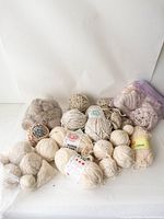 Assorted balls and skeins of neutral colored wool yarns and acrylic blends.