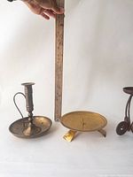 Photo of three brass candle holders together with a ruler for size comparison, showing various styles and patina.