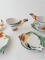 Photo shows 2 butterfly handle ceramic teacups and 4 matching butterfly decorated saucers with leaf shaped edges and bright colors