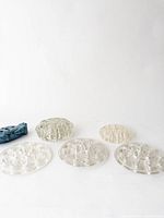 Photo showing five clear glass round flower frogs in various sizes and patterns arranged on a white surface.