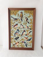 Full view of framed tea towel depicting multiple bird species with names and yellow autumn leaves on a blue background.
