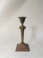 Full candlestick showing its overall form and triangular stem topped with a flared candle holder cup.